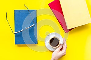 Reading books in library with glasses and coffee in hands on yellow background top view