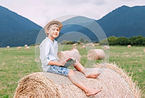 Reading boy sits over the haystack roll on the mountain field