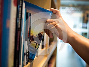 Reading concept. male hand choosing and picking book in a bookshelf. Book Travelogue, education research and self learning