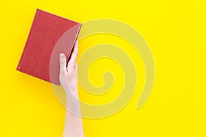 Reading concept. Reading as hobby. New knowledge. Hands take hardback book with empty cover on yellow background top