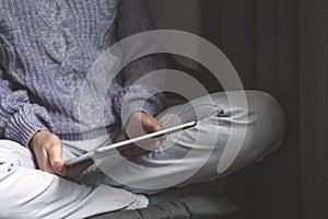 Reading concept. Young woman using tablet pc relaxing in cozy house, sitting on chair. Front view, selective focus photo