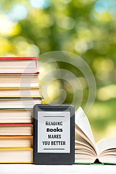 Reading. E-book reader and a stack of books. The park is blurred in the background. Copy space. Vertical. Concept of education and