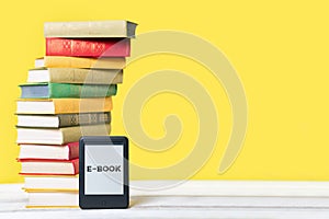 Reading. E-book reader and a stack of books on a yellow background. Copy space. Concept of education and electronic gadgets