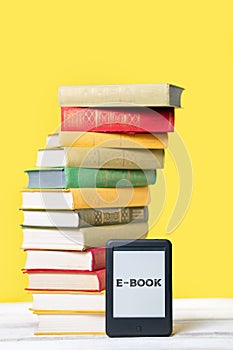 Reading. E-book reader and a stack of books on a yellow background. Vertical. Copy space. Concept of education and electronic