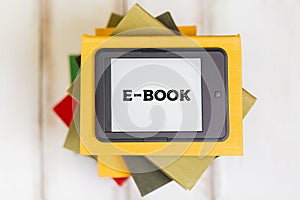 Reading. E-book reader is on top of a stack of books on a wooden background. Flat lay. Concept of education and electronic gadgets