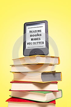 Reading. E-book on top of a stack of books on a yellow background. Vertical. Concept of education and electronic gadgets