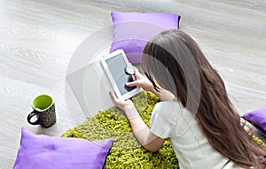 Reading e-books. little girl reading e-book while lying on the floor.