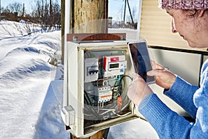 Reading electricity meter in outdoor switchboard in winter, using smartphone.