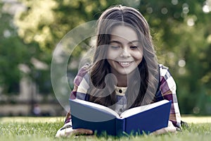 Reading only enhances your knowledge. Happy child read book lying on green grass. School library. Imagination and