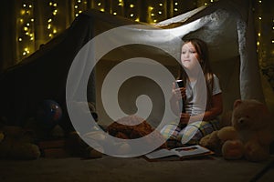 Reading and family games in children& x27;s tent. Little girl with books and flashlight before going to bed