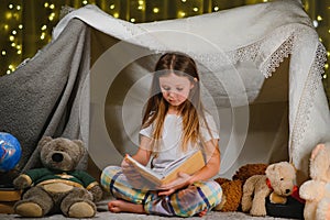 Reading and family games in children& x27;s tent. Little girl with books and flashlight before going to bed