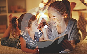 Mother and child daughter reading a book and a flashlight before