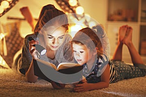 Mother and child daughter reading a book and a flashlight before