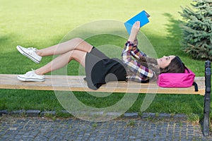 Reading is fun. Happy child read book lying on park bench. School library. Imagination and fantasy. Literacy education