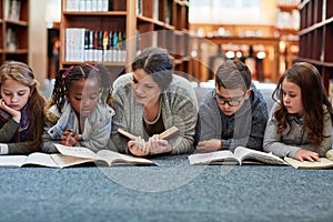 Reading is fundamental. Cropped shot of elementary school kids reading with their teacher on the floor in the library.