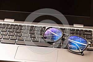 Reading glasses with coating filter to prevent Computer Vision Syndrome CVS sit on laptop keyboard. Concept of digital eye