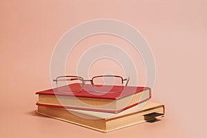 Reading glasses lie on a stack of old worn books on a colored background