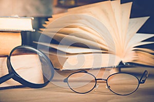 Reading glasses and magnifying glass with olds book on table.