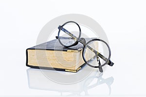 Reading glasses on old book on white background