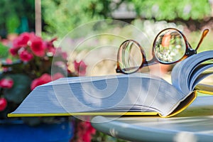 Reading glasses and open book on table in garden