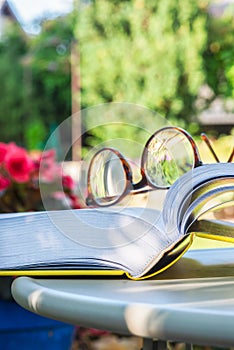 Reading glasses and open book on table in garden