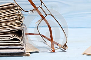 Reading glasses and stack of newspapers on a blue wooden shelf