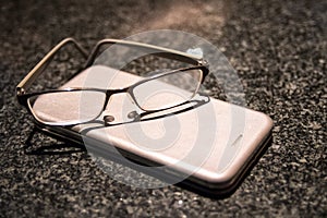 Reading glasses on top of a mobile phone on a marble table top
