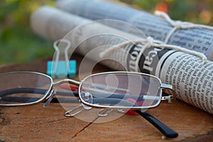 Reading glasses on a wooden table next to the newspapers sign of a business layout