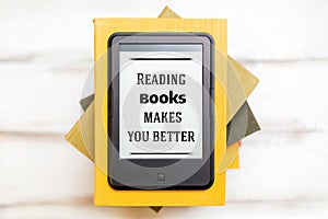 Reading and knowledge. E-book reader is on top of a stack of books on a wooden background. Flat lay. Concept of education and