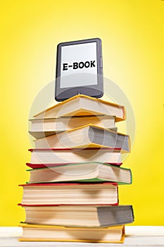 Reading and knowledge. E-book on top of a stack of books on a yellow background. Vertical. Concept of education and electronic