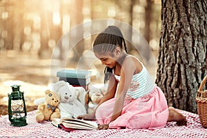 Reading lights up their imaginations. a little girl reading a book with her toys in the woods.