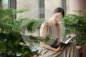 Reading, plants and woman in home with book to relax with glamour, comfort and elegant fashion. Eco, green decor and