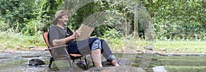 Reading or study concept A happy bearded Asian man sits alone in a chair near a stream in the countryside and enjoys