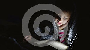 Reading teen girl child reads book reading at night with flashlight lying a under blanket