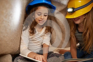 Reading their favorite stories. two little girls reading underneath a blanket using headlamps.