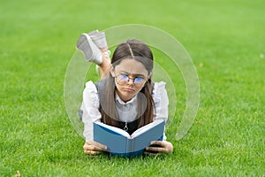 Reading time. Frown teenage girl reading book lying on grass after school, reading