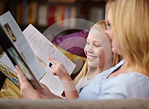 Reading together. A cute young girl sitting next to her mother while they read a book.