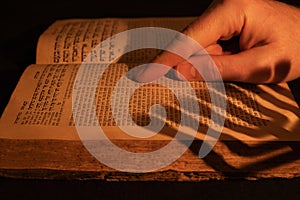 Reading Torah. Male hand on old Hebrew Bible in candle light. Shadow from menorah on open Jewish prayer book in the dark