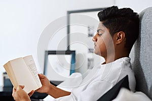 Reading is the only way you can travel while being home. a young man reading a book while lying on his bed.