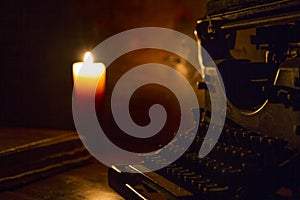 Reading and writing scenes in ancient times: an old book and an old typewriter on a ruined wooden table lit by a candle on a woode