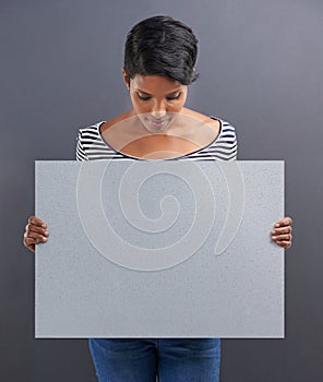 Reading your copy. Studio shot of a beautiful young woman holding a blank placard against a grey background.