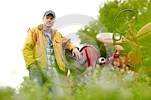 Ready for another day in the felds. Portrait of handsome farmer leaning on the tyre of his tractor in a field.