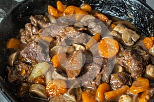 Ready of Beef Burgeoning beef dish in a frying pan. meat, carrots and onions and mushrooms. Appetizing sauce. Slow food