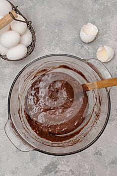 Ready dough for making chocolate sponge cake for roll in a bowl on a gray concrete background. Recipe step by step.