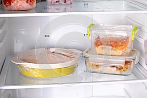 Ready frozen food in containers and in a baking dish on the refrigerator shelf