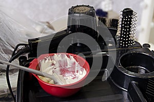 Ready-made hair dye in a container, a black hairdryer and professional hair brushes on a special table in a hairdressing salon