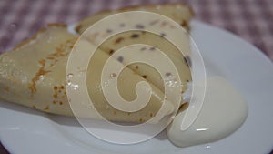 Ready-made pancakes in a plate with sour cream.