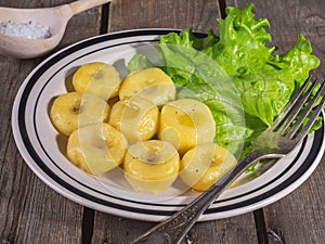 Ready-made potato gnocchi with leaves of fresh leaf lettuce on a ceramic plate with stripes, shot from close range on a plank