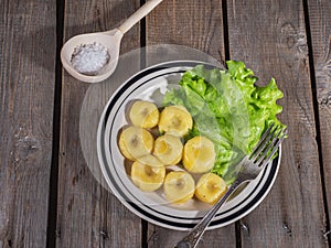 Ready-made potato gnocchi with leaves of fresh leaf lettuce on a ceramic plate with stripes, a table fork and a spoon on a plank