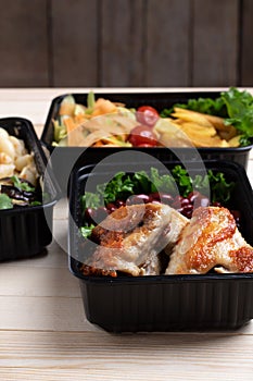 Ready meals to eat, containers with fried chicken wings and raw vegetables on rustic background, cherry tomato  and micro greenss